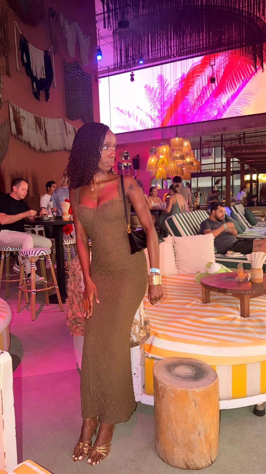 ZuriNiah standing full length in an olive lace dress and gold heels in a night venue