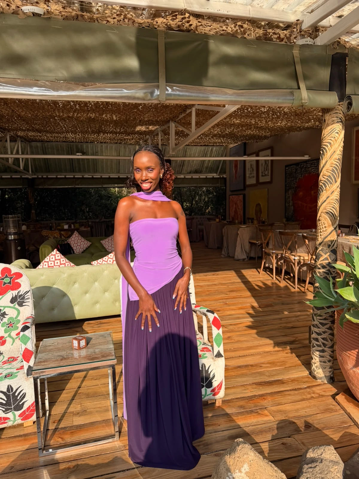 ZuriNiah standing beneath a thatched canopy in a strapless lilac top and a long deep-purple skirt